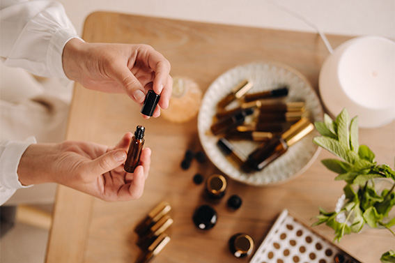 2 mains qui manipilent un roll-on d'huile essentielle au dessus d'une table en bois avec plusieurs roll-on